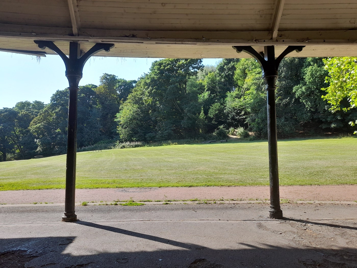 A view over a green field and trees from under a wooden pavillion
